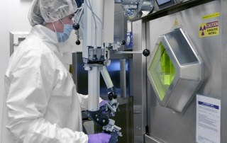 Un homme en tenu de laboratoire, avec gants, masque et charlotte, netrain d'utiliser une machine pour controler le produit radioactif